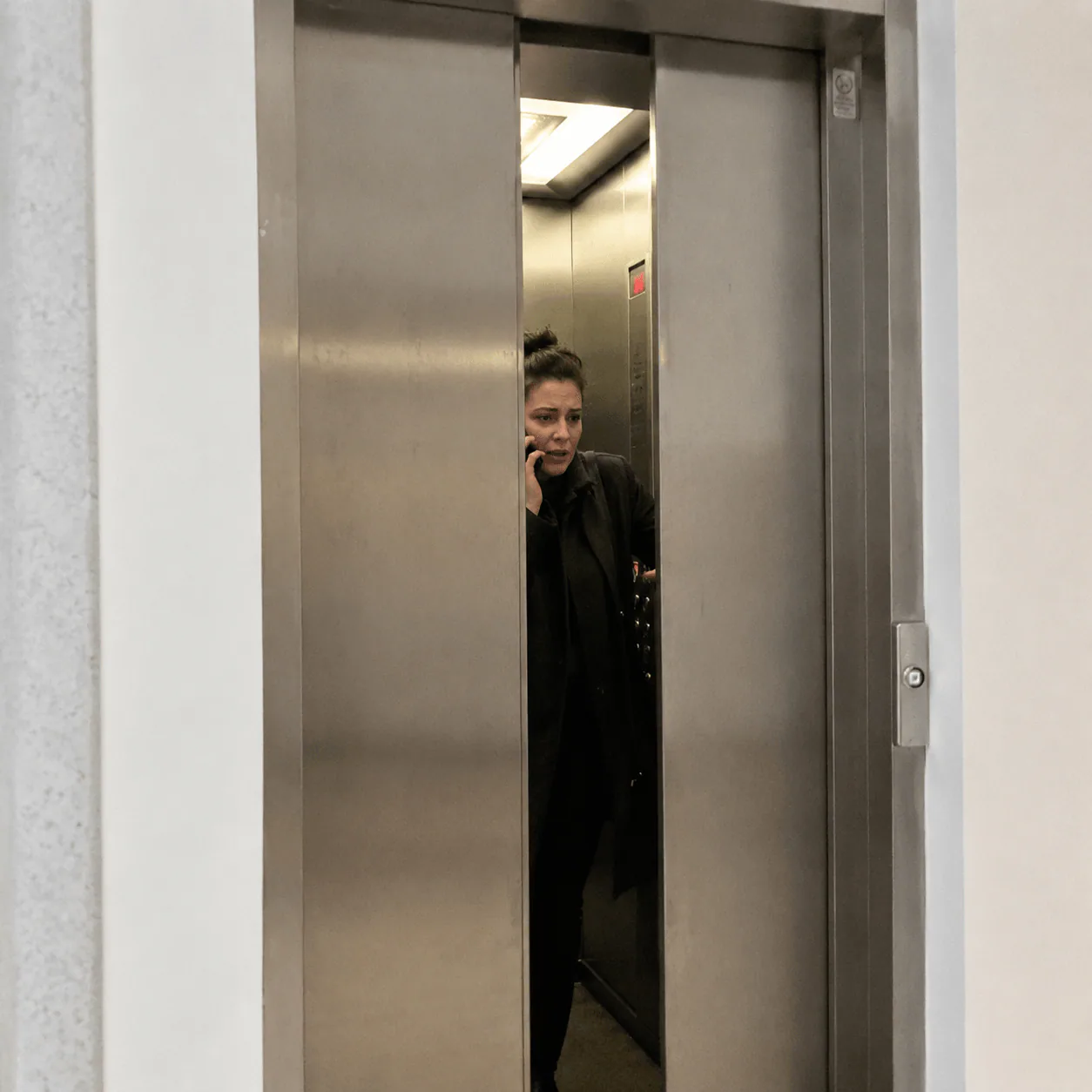 person trapped in elevator looking worried pressing emergency button, modern elevator interior, emergency situation, realistic photo